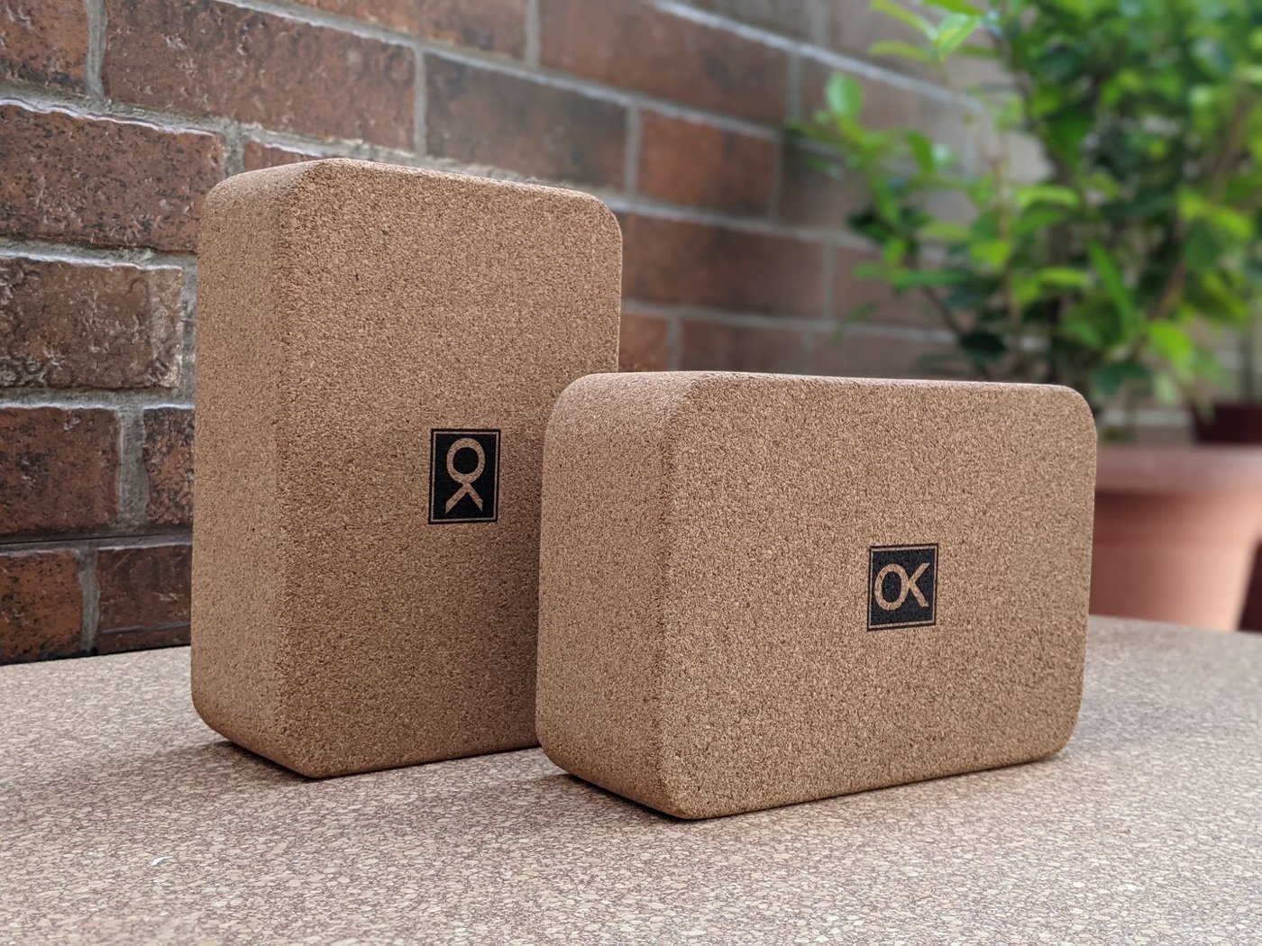 An OKACK! cork yoga block resting against a brick wall